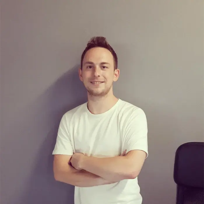Nikos Papageorgiou smiling, arms crossed, against a grey wall